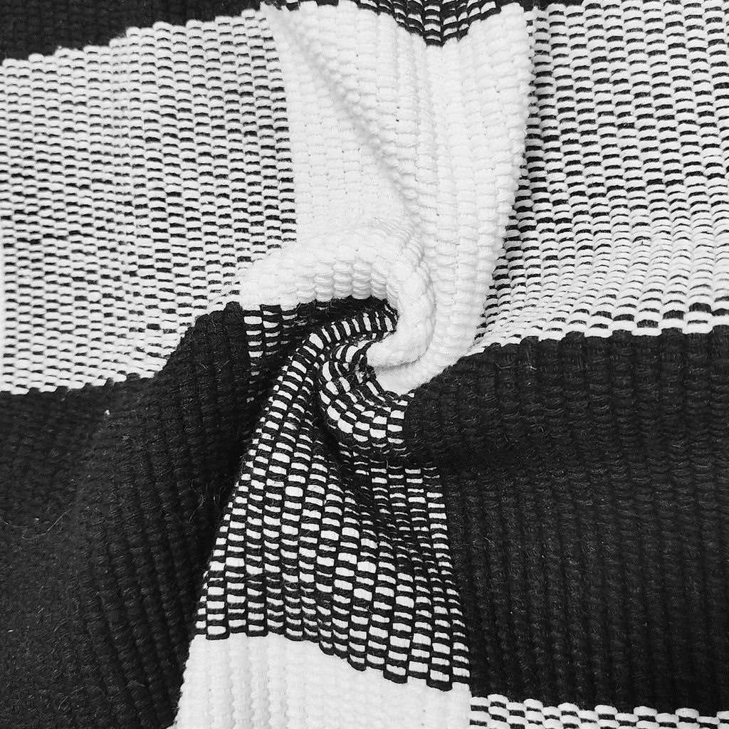 Close-up of a black and white buffalo plaid woven rug with a section curled to show texture.