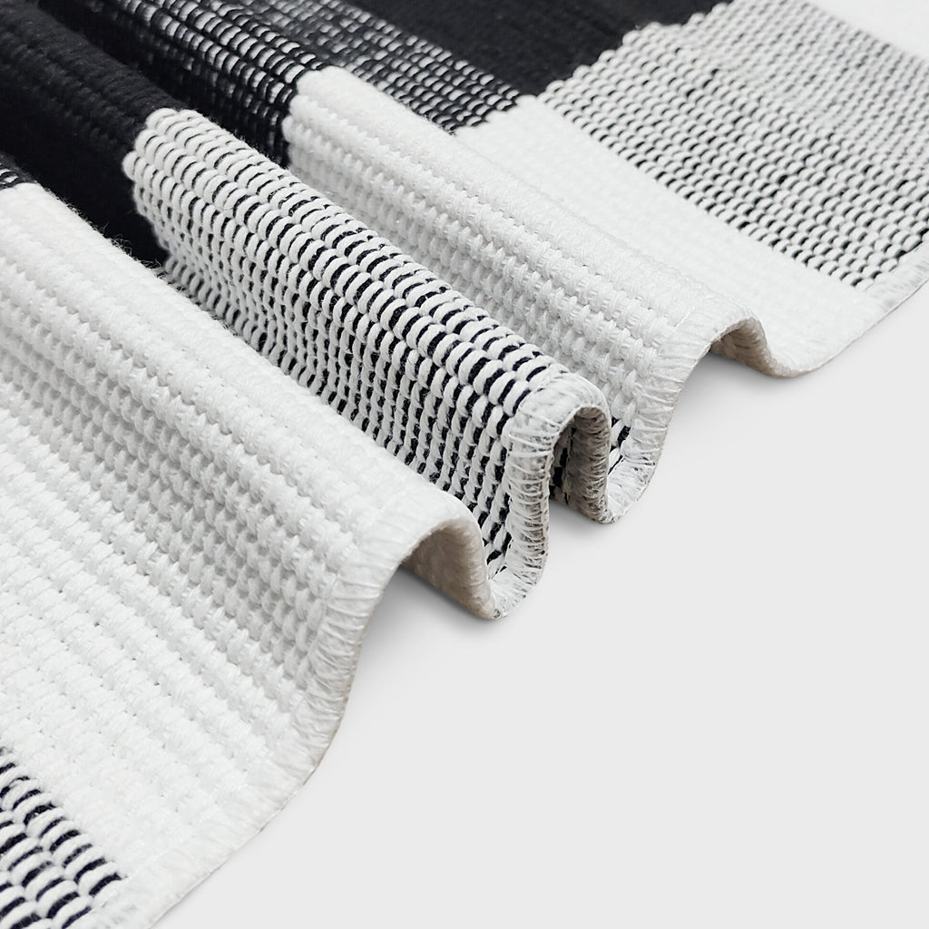 Close-up of a black and white buffalo plaid woven rug showing texture and weave detail.