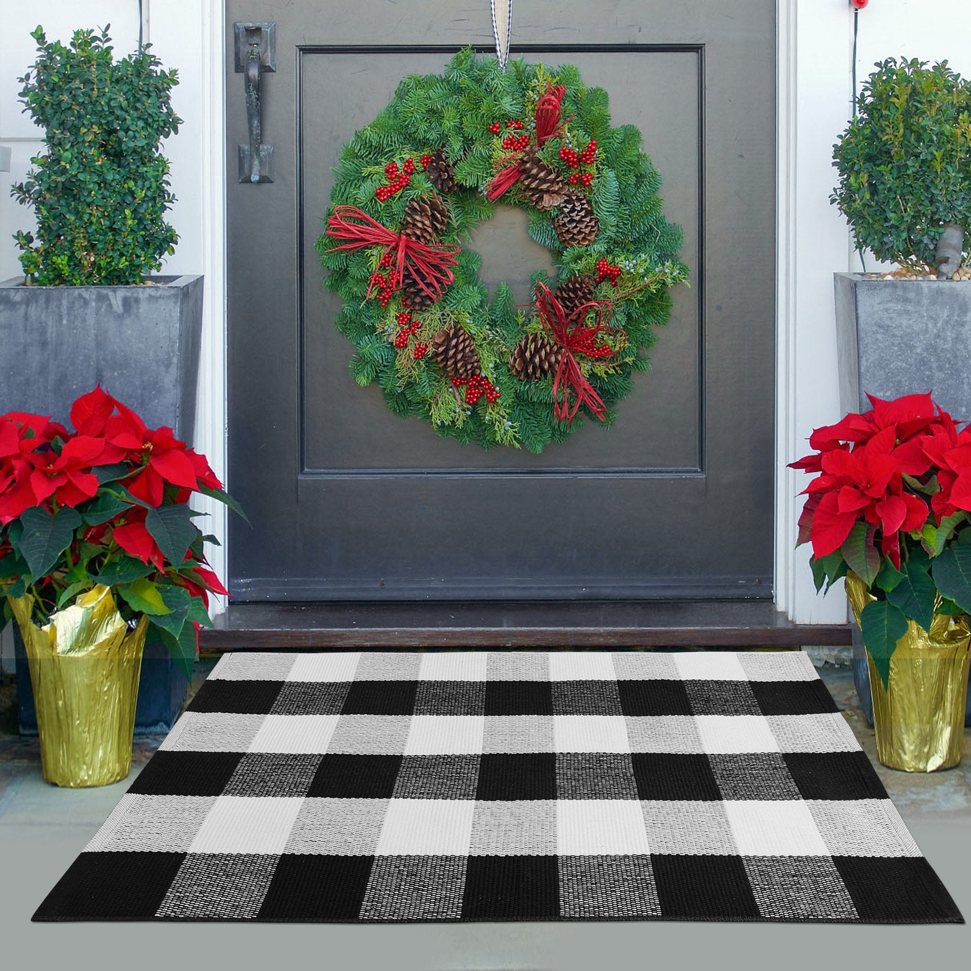 Black and white buffalo plaid outdoor rug on a doorstep with poinsettias and a Christmas wreath