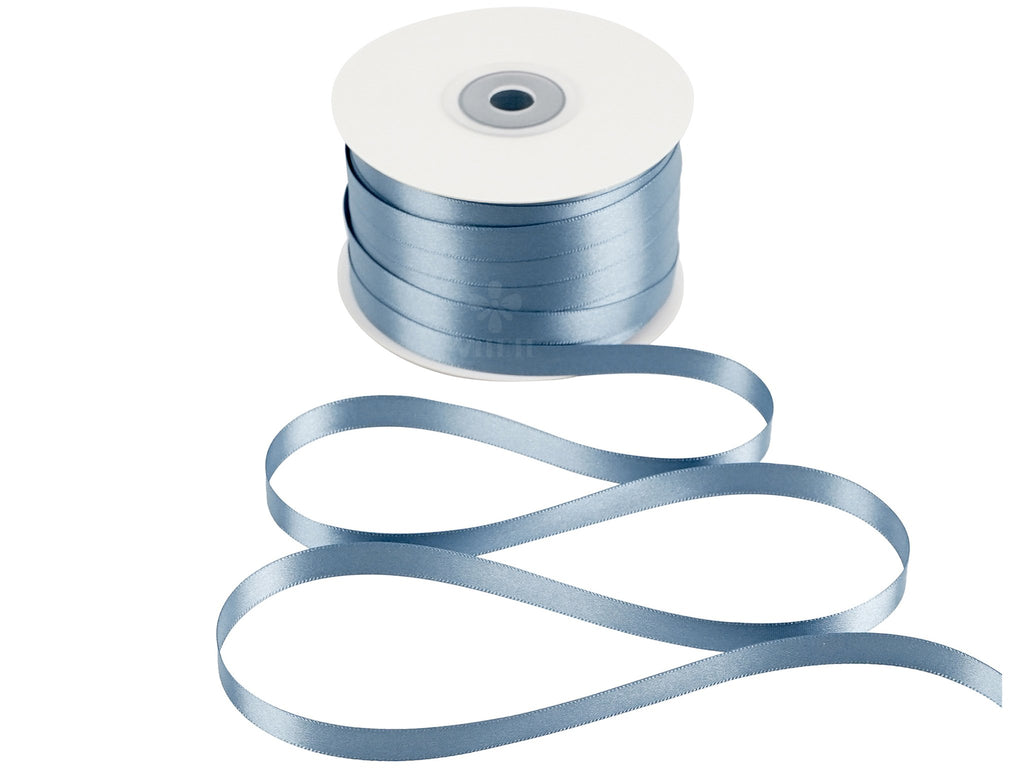 Spool of dusty blue double sided satin ribbon with ribbon unspooling in a wavy pattern on a white background.