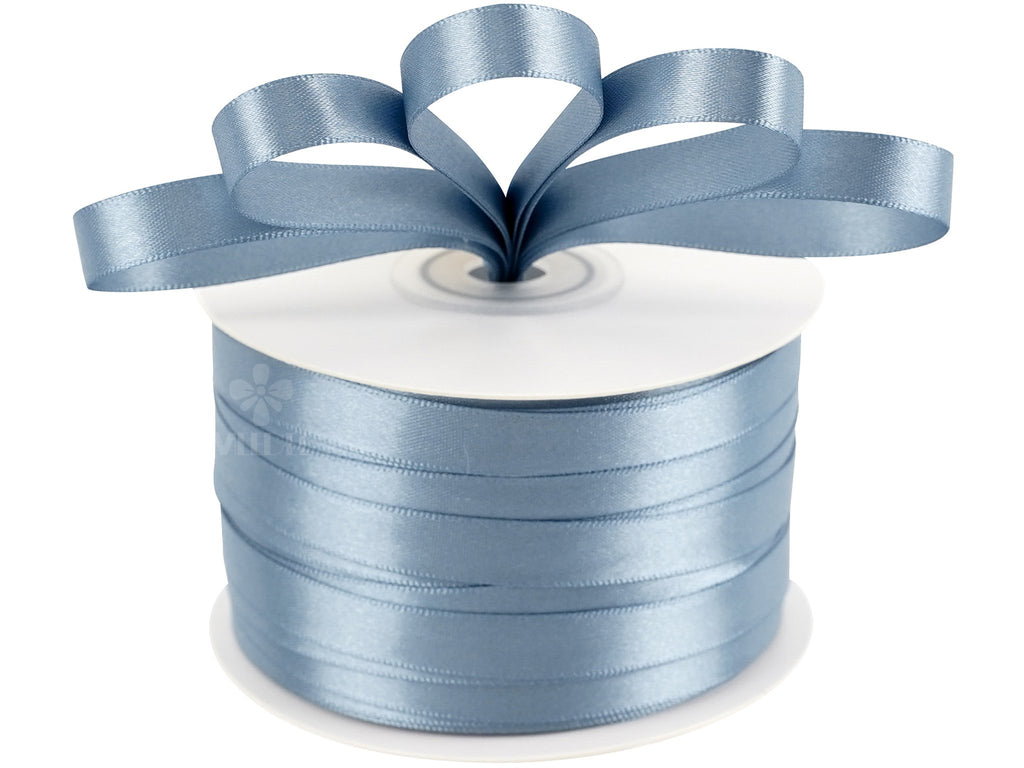 Spool of dusty blue double sided satin ribbon with a bow tied at the top, isolated on white.