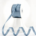 Spool of dusty blue double-sided satin ribbon with a length of ribbon unspooled in a wavy pattern.