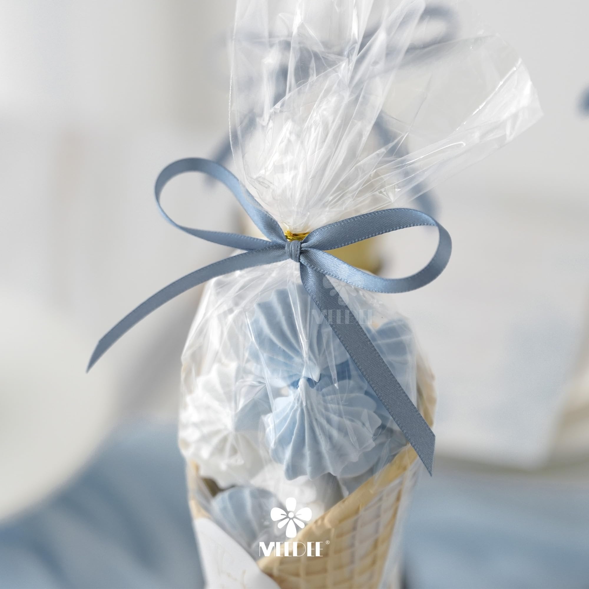 Dusty blue satin ribbon tied around a clear plastic bag filled with meringue cookies in a waffle cone.