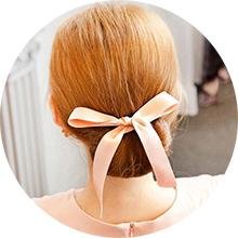 Back of woman's head with blonde hair styled up and tied with a peach satin ribbon bow