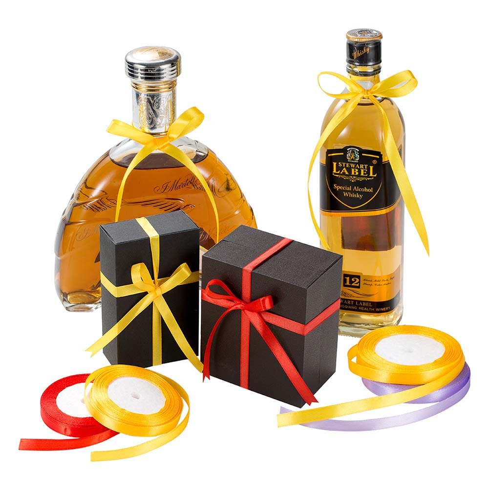 Two bottles of alcohol and two gift boxes decorated with satin ribbons, with spools of ribbon in the foreground.