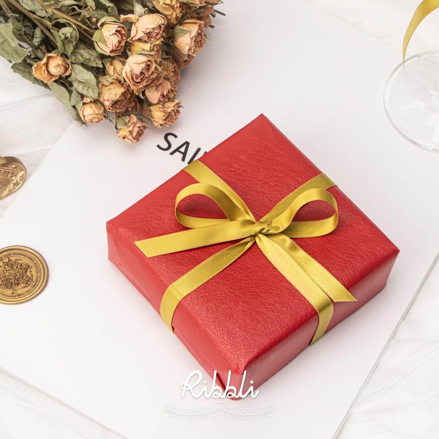 Red gift box with gold ribbon and dried flowers on a white surface