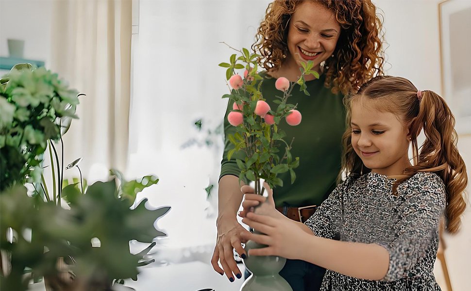 Woman and child arranging artificial peach branches with pink fruit in a vase
