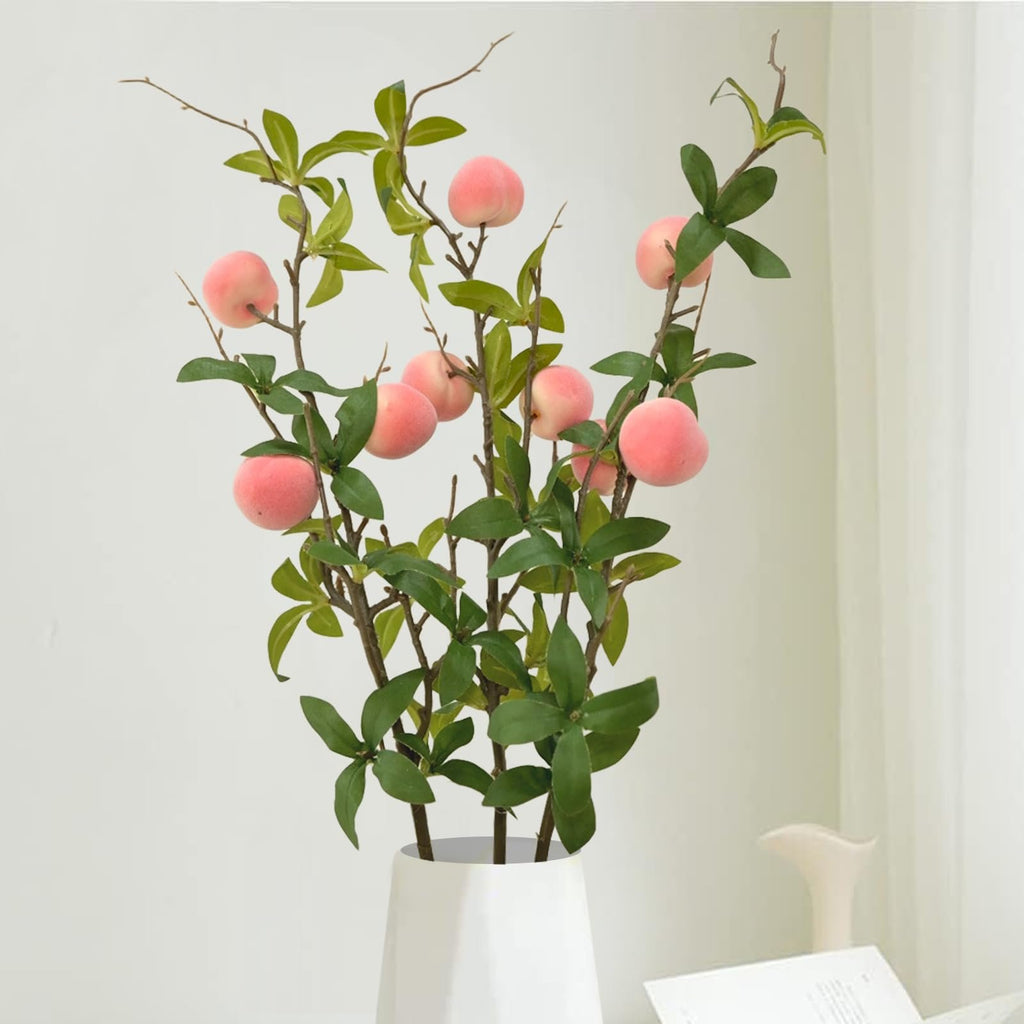Three bunches of artificial peach branches with pink peaches and green leaves in a white vase.