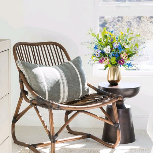 Rattan chair with a striped pillow and a vase of colorful artificial wildflowers on a side table.