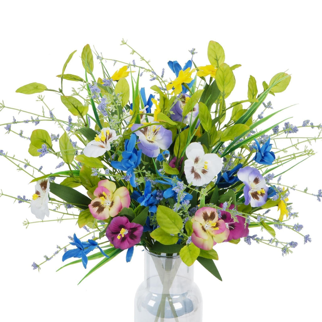Mixed artificial pansy and wildflower bouquet in a clear glass vase, featuring purple, pink, yellow, blue, and white flowers with green foliage.
