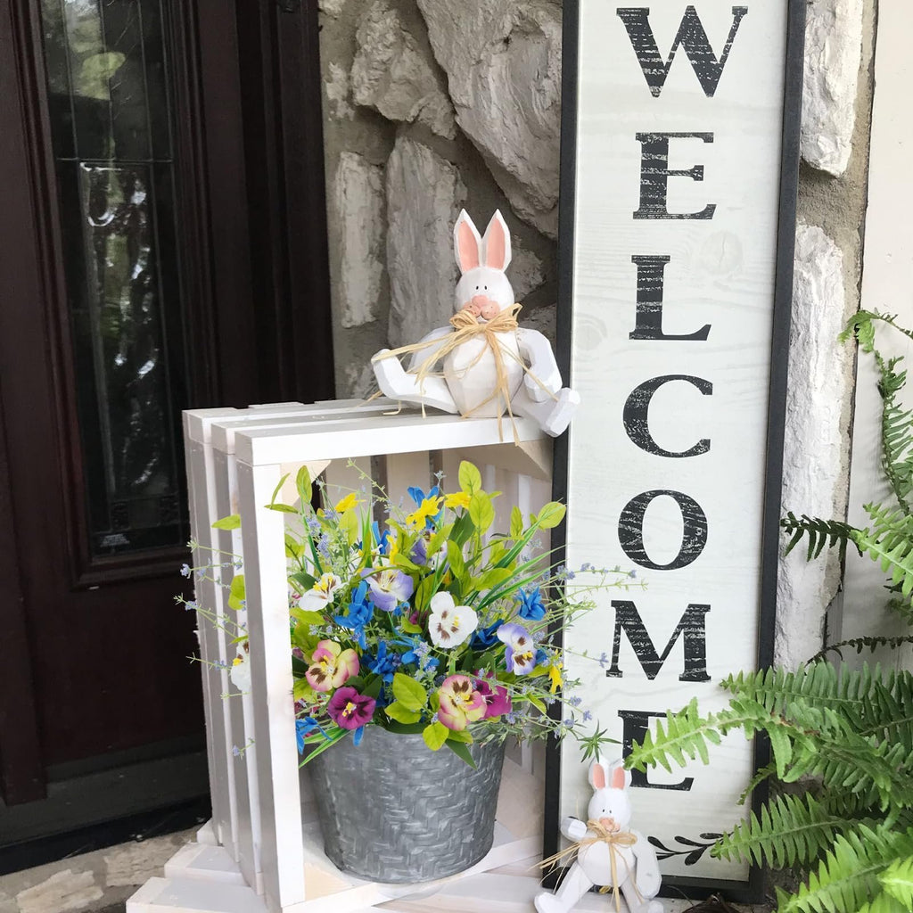 Artificial mixed pansy wildflower bouquet in a galvanized pot next to a welcome sign and decorative bunnies.
