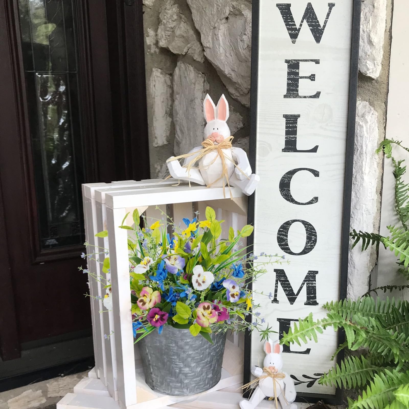 Artificial mixed pansy wildflower bouquet in a galvanized pot next to a welcome sign and decorative bunnies.