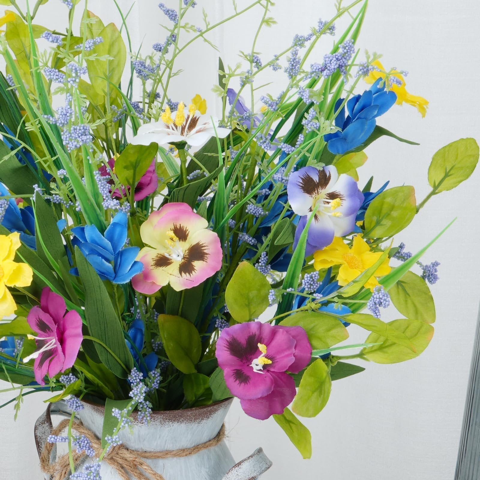Close-up of a colorful artificial wildflower bouquet with pansies, blue flowers, and yellow accents in a rustic vase.