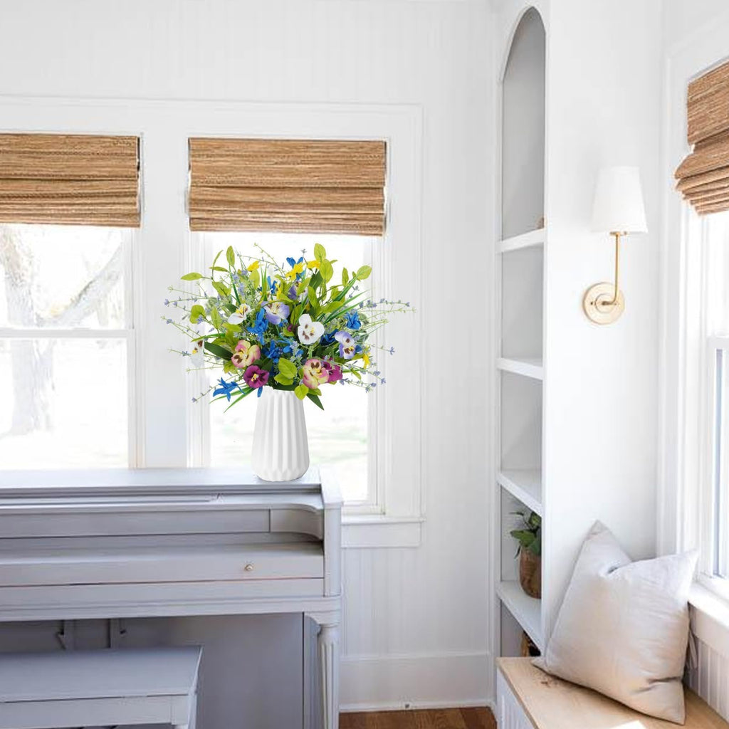 Mixed artificial pansy and wildflower bouquet in a white vase on a piano