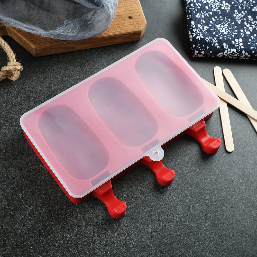 Red silicone popsicle mold with lid and three oval cavities, with wooden sticks on the side.