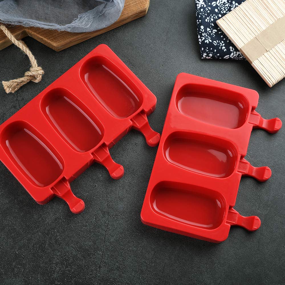 Two red silicone popsicle molds with oval cavities and stick holders, shown on a dark surface with wooden sticks and fabric in the background.