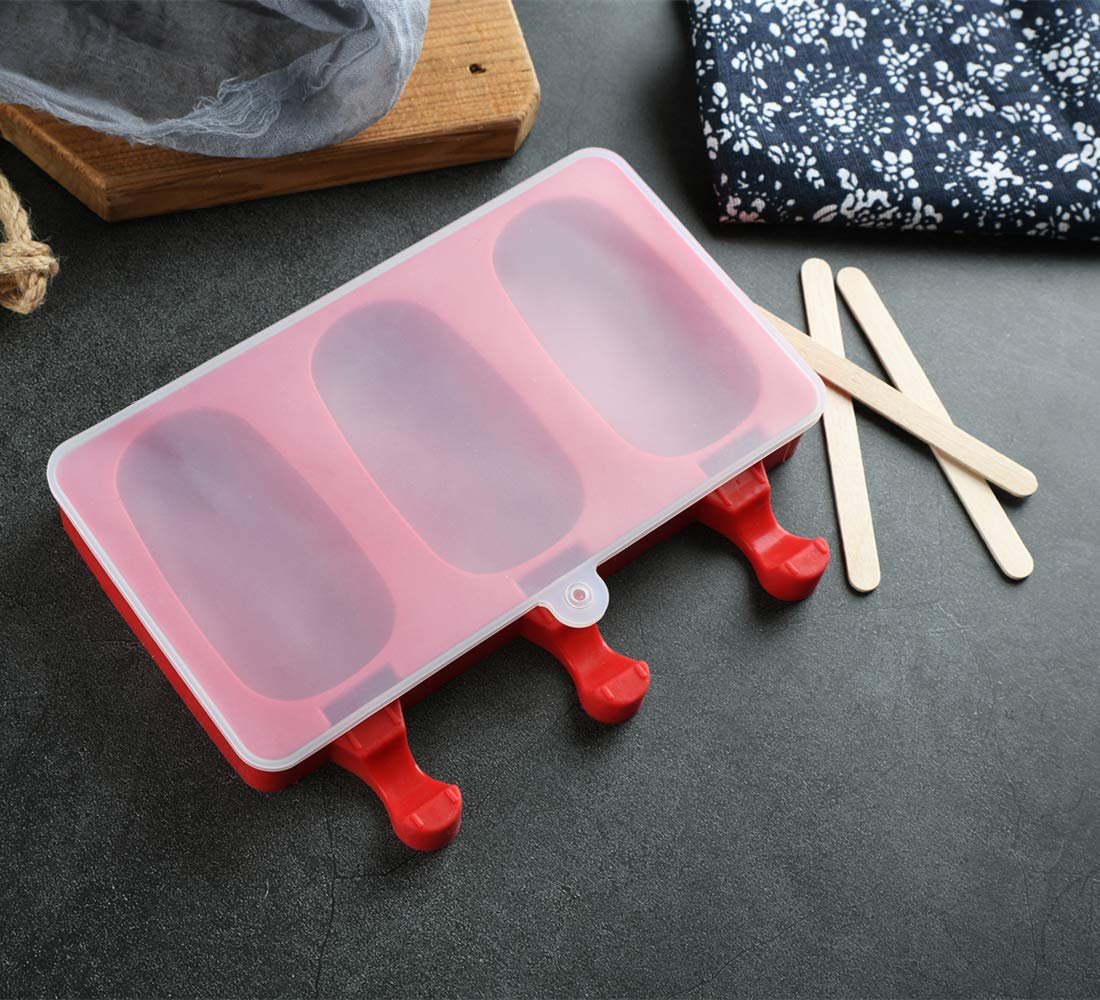 Red 3-cavity silicone popsicle mold with a clear lid and wooden sticks on a dark surface.