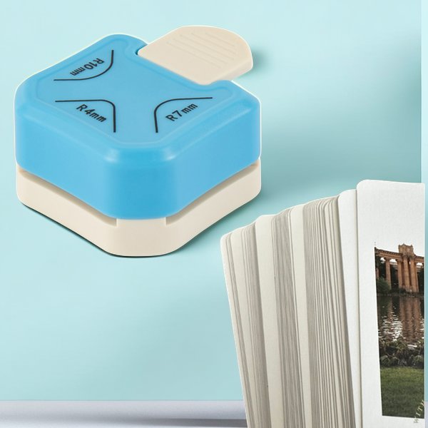 Blue and cream 3-in-1 paper corner rounder punch with R4mm, R7mm, R10mm markings next to a stack of photos on a light blue background.