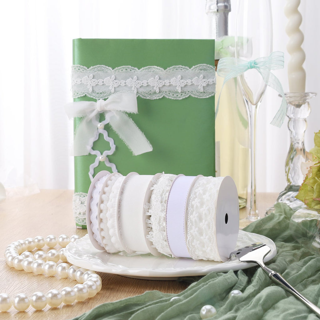Assortment of white ribbons on spools, displayed on a white plate with pearls and a green decorative cloth.