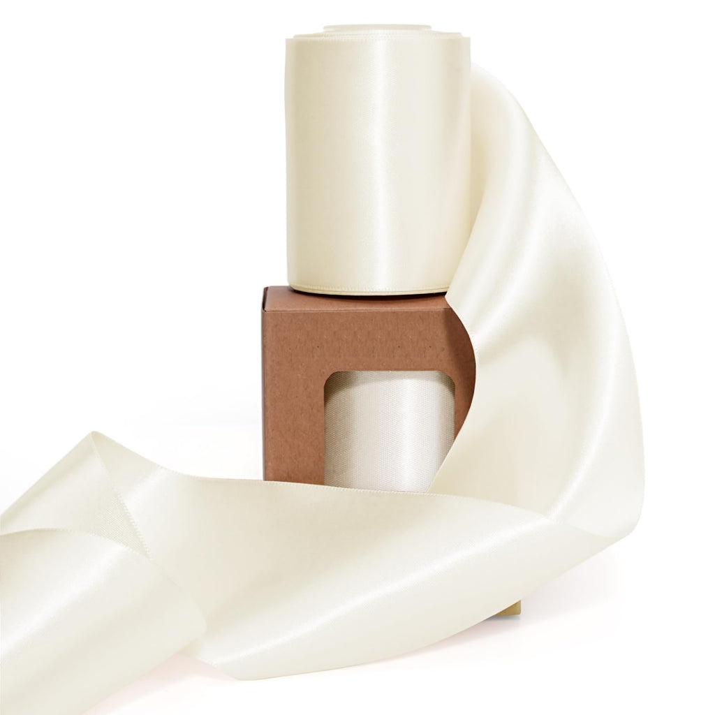 Two spools of ivory double-faced satin ribbon on a brown cardboard box, with ribbon unfurled in foreground