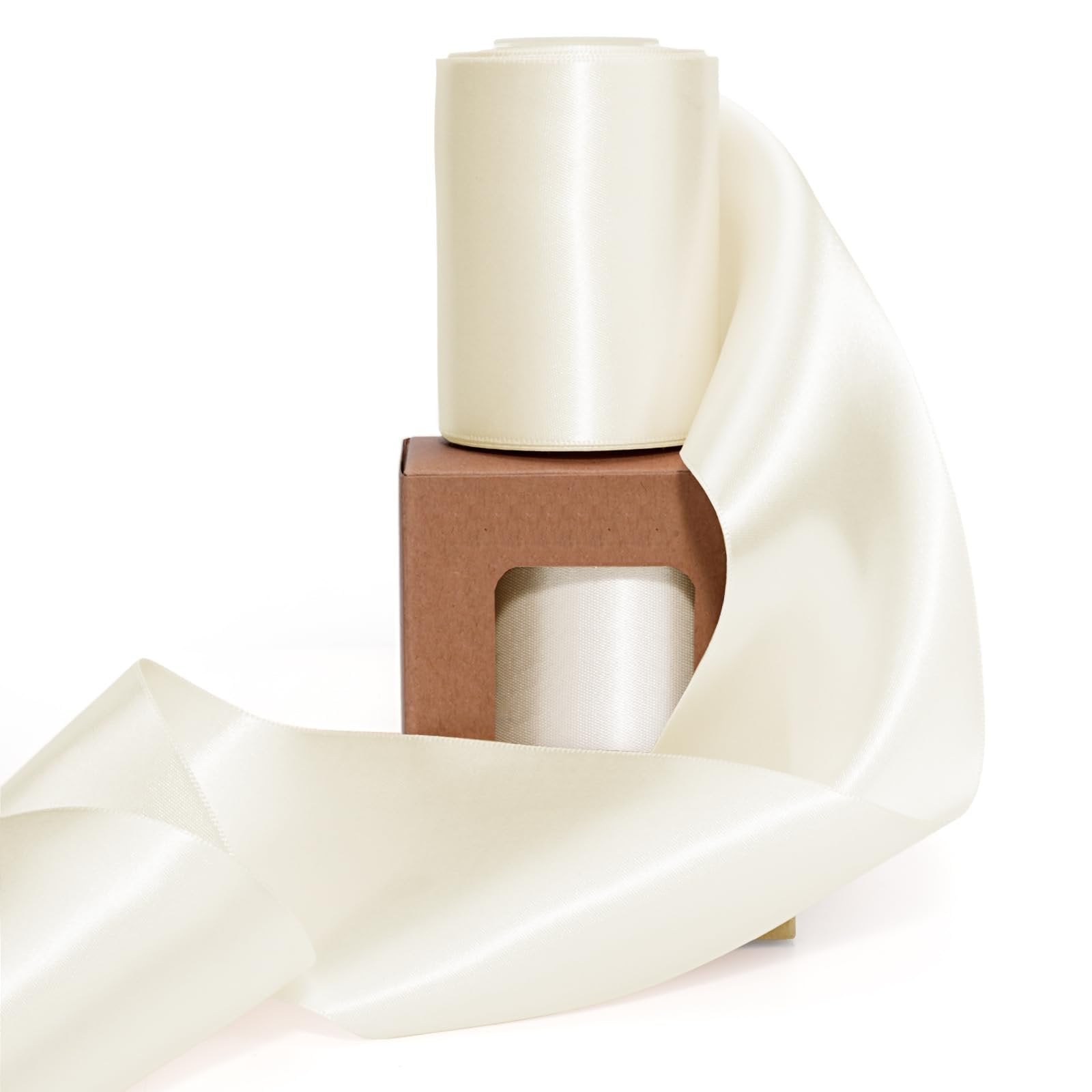 Two spools of ivory double-faced satin ribbon on a brown cardboard box, with ribbon unfurled in foreground