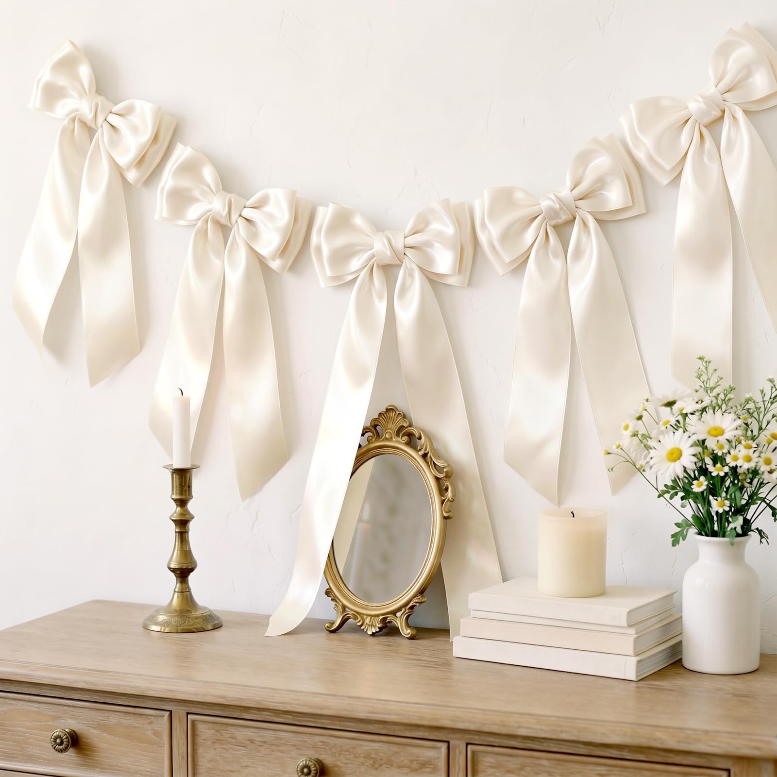Ivory double-faced satin ribbon bows arranged as a garland on a white wall above a wooden dresser.