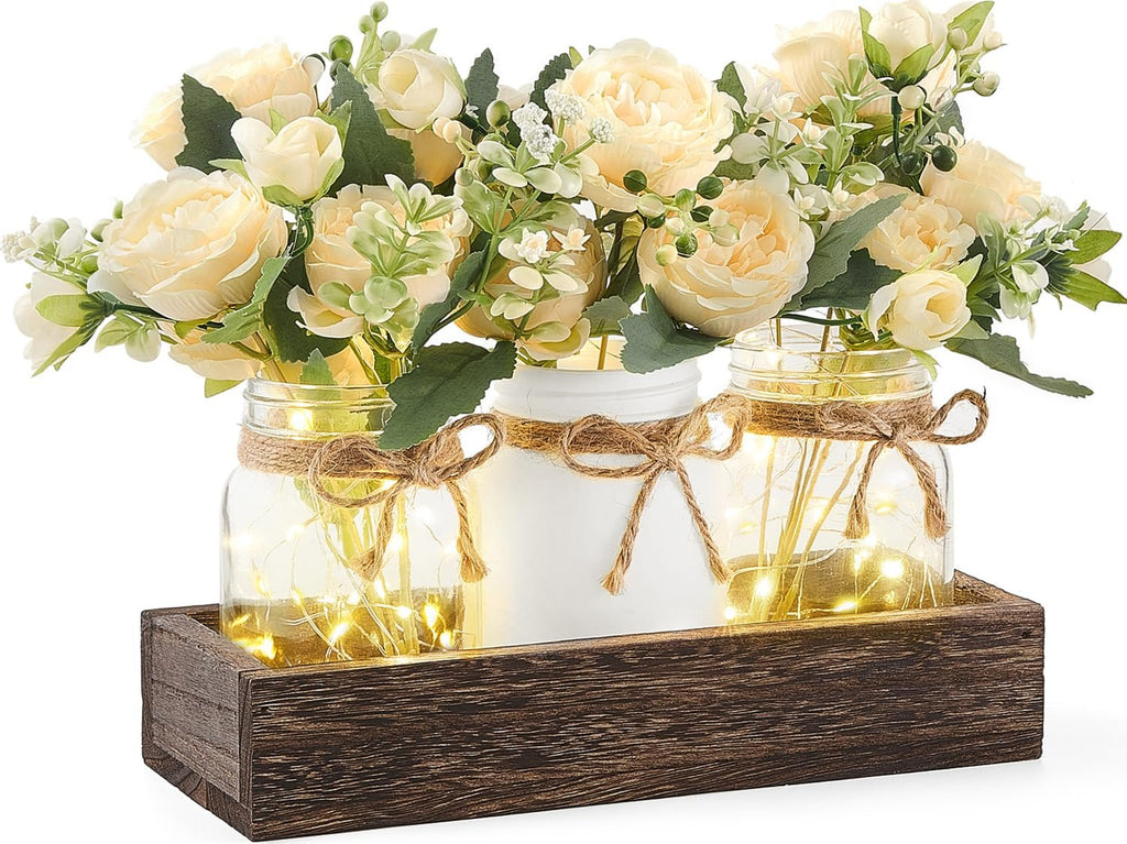 Three mason jars with artificial flowers and string lights in a wooden tray, farmhouse decor