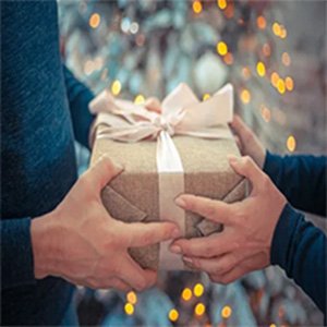 Two people exchanging a wrapped gift with a pink bow, festive bokeh lights in background