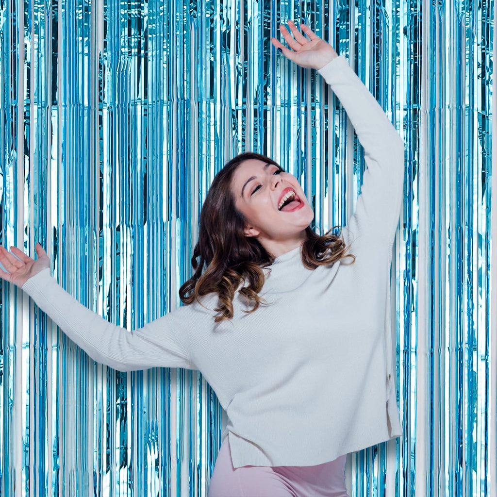 Woman laughing with arms raised in front of a light blue foil fringe backdrop