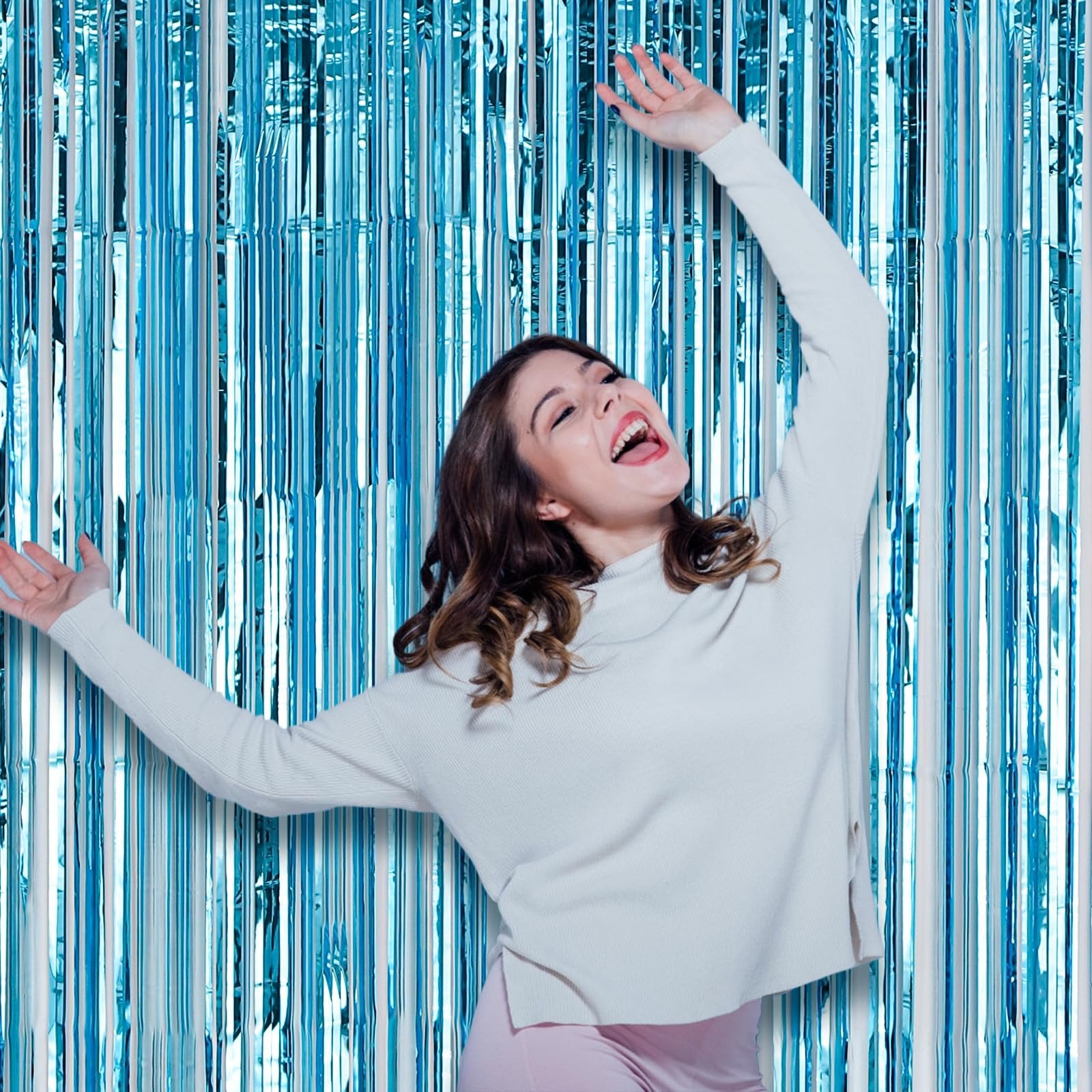 Woman laughing with arms raised in front of a light blue foil fringe backdrop