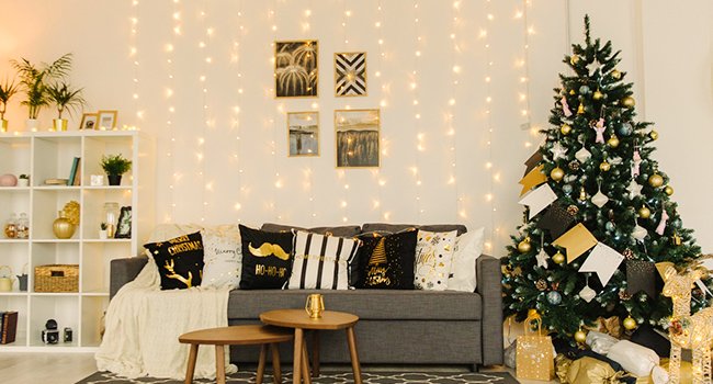 Living room decorated for Christmas with a decorated tree, sofa with festive pillows, and string lights on the wall.