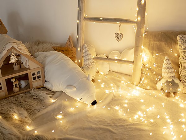 Cozy winter scene with fairy lights, a wooden dollhouse, a polar bear plush, and gnomes.