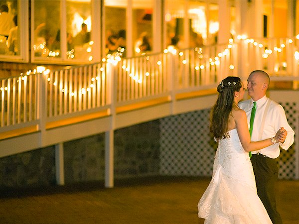 Wedding couple dancing on a deck with warm white fairy lights strung along the railing and building.