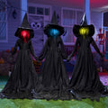 Three light-up flying witch yard stakes with flashing LED heads in red, blue, and yellow, holding hands on a lawn at dusk.