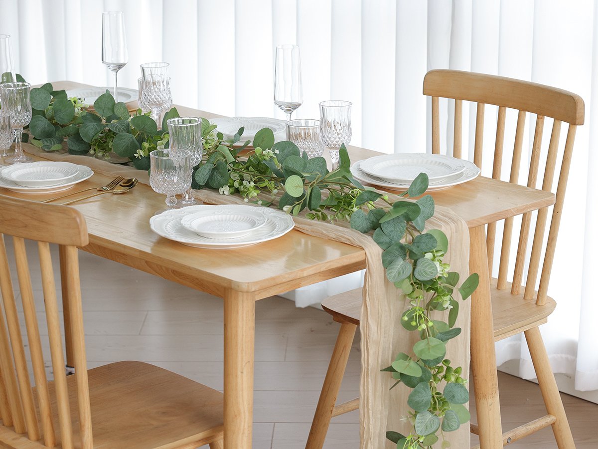 Table setting with artificial eucalyptus garland draped over a runner, plates, glasses, and cutlery.