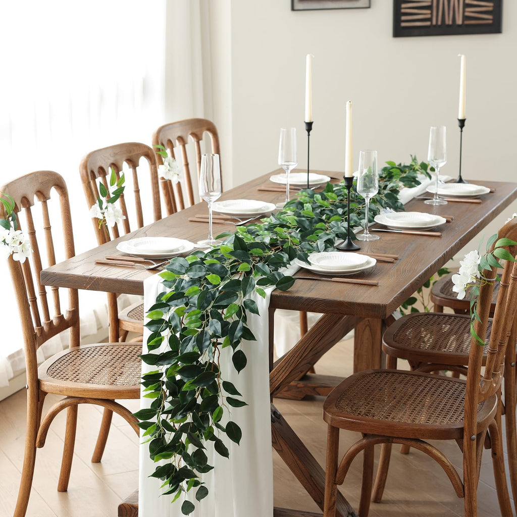 Dining table set with artificial ficus vine garland, plates, glasses, and candles