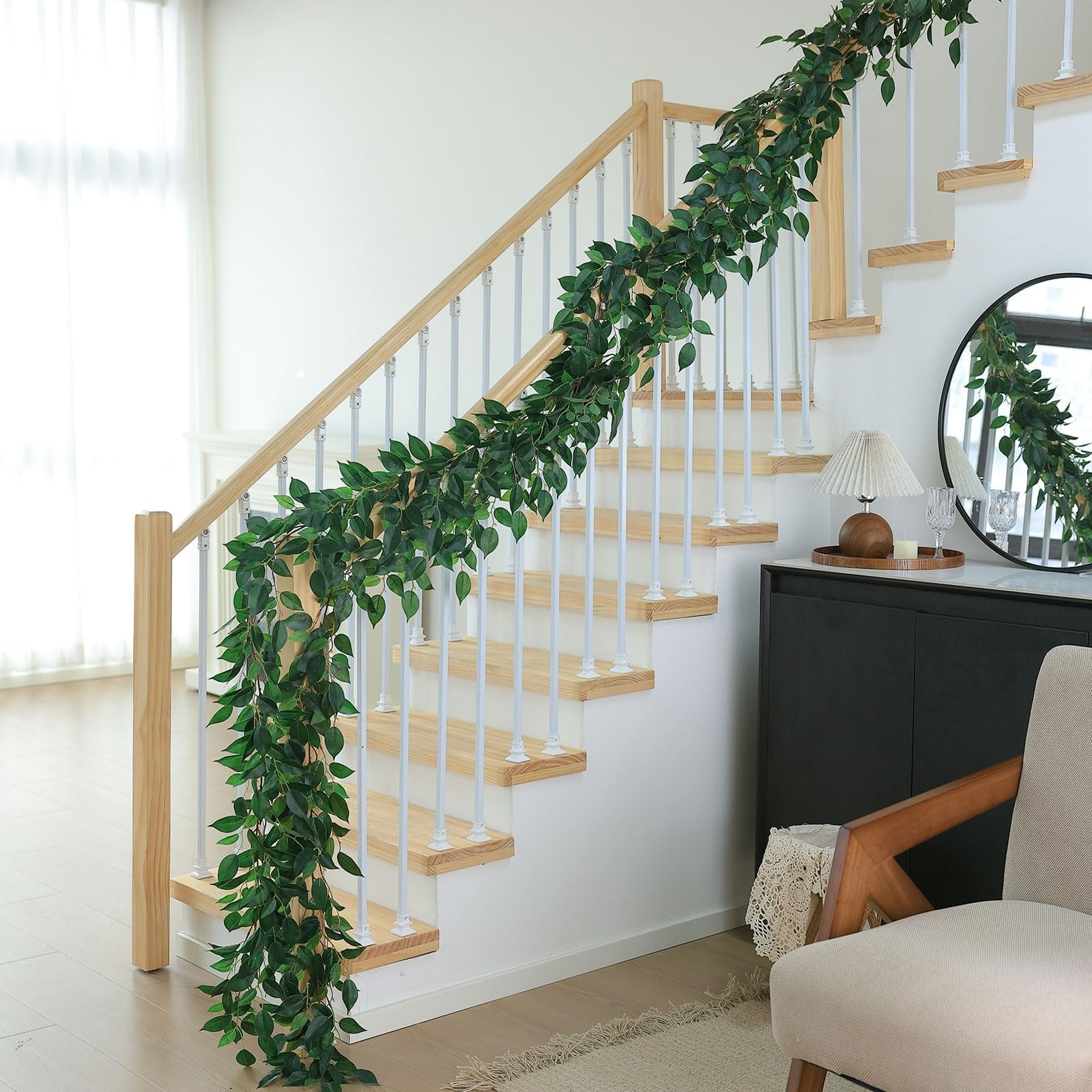 Artificial ficus vine garland draped along a wooden staircase railing with white spindles.