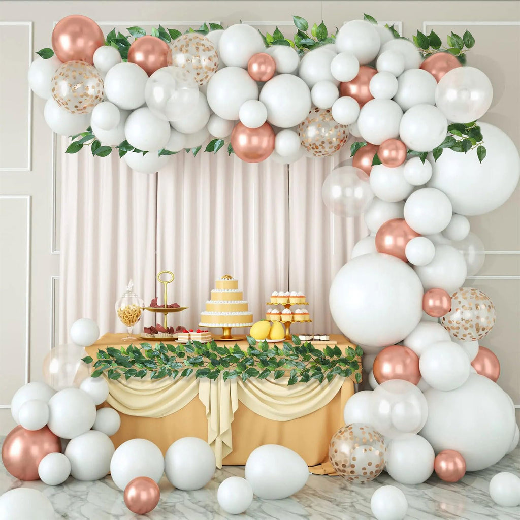 White and rose gold balloon garland arch over a dessert table with a cake and cupcakes
