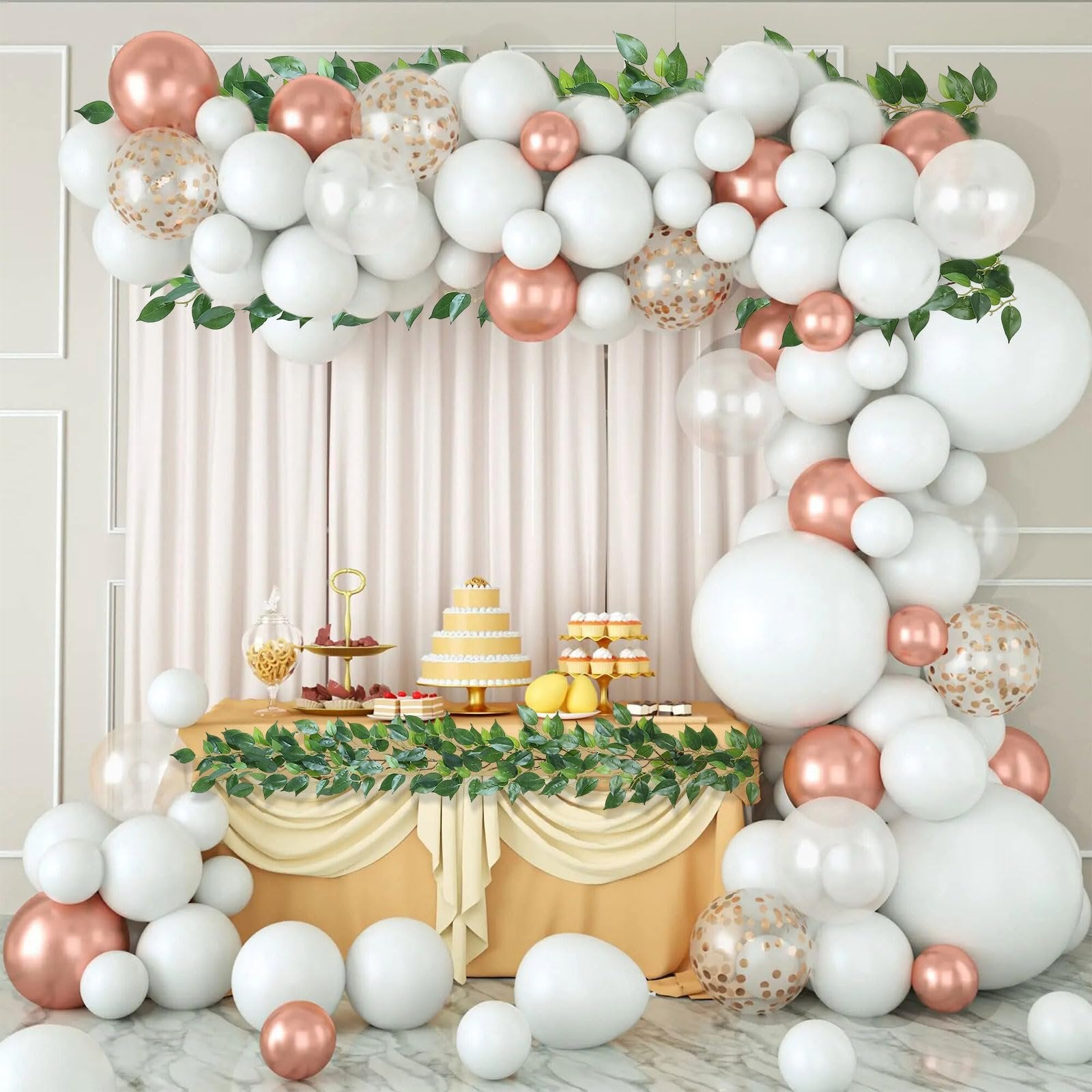White and rose gold balloon garland arch over a dessert table with a cake and cupcakes