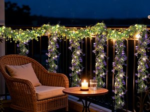 Artificial eucalyptus garland with purple flowers and LED lights draped on a balcony railing at night