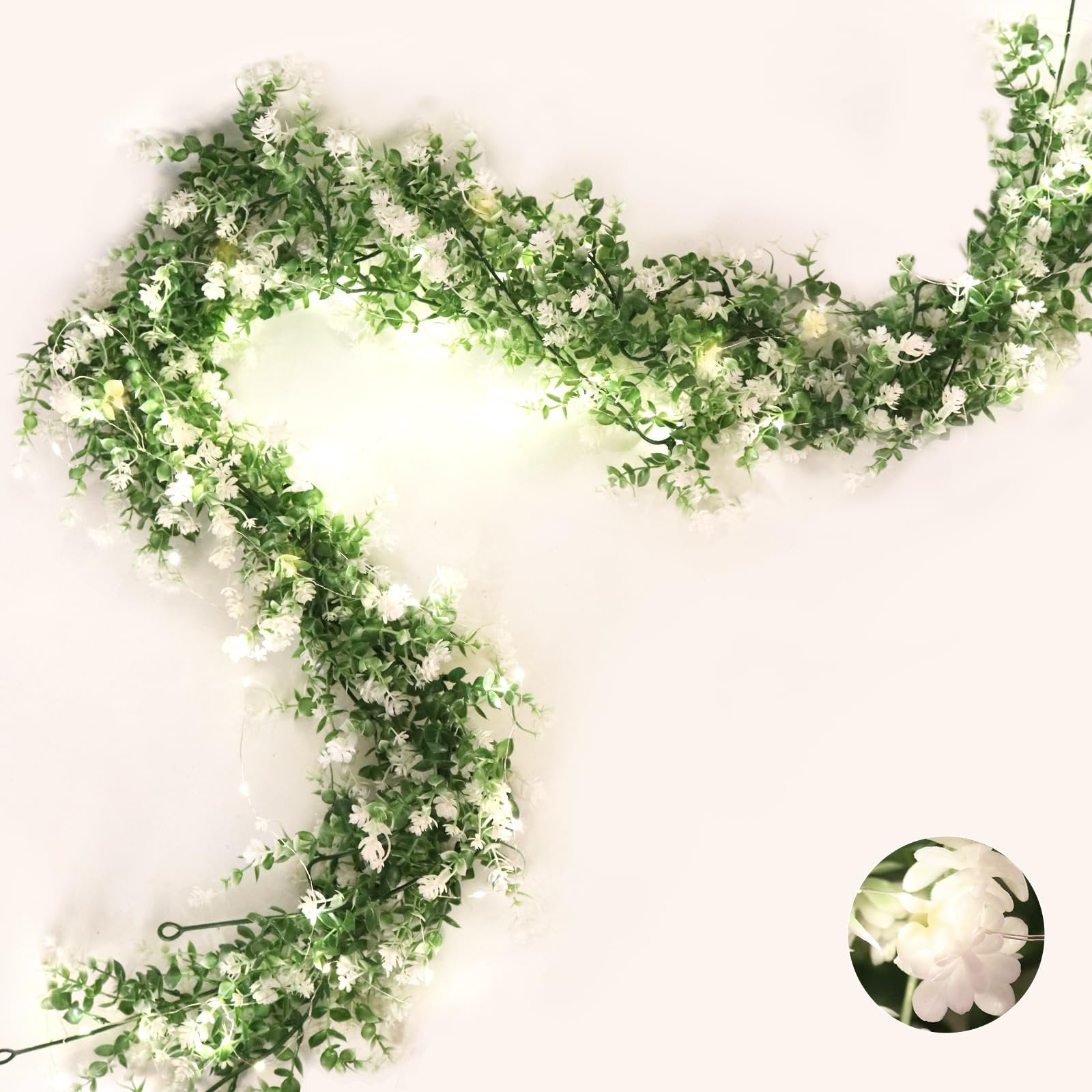 Artificial eucalyptus garland with small white flowers and LED lights draped on a white background