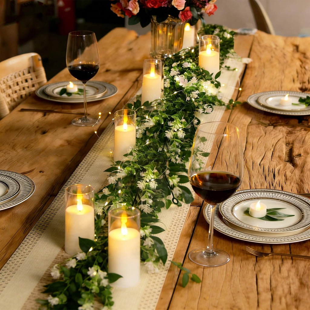 Table setting with artificial eucalyptus garland, LED lights, candles, wine glasses, and plates