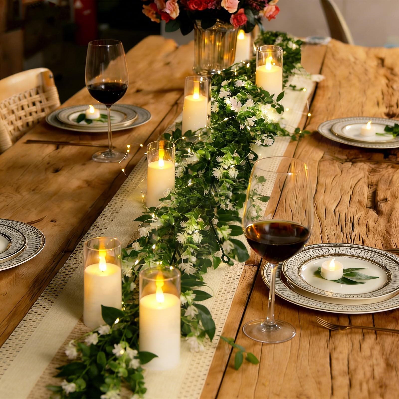 Table setting with artificial eucalyptus garland, LED lights, candles, wine glasses, and plates