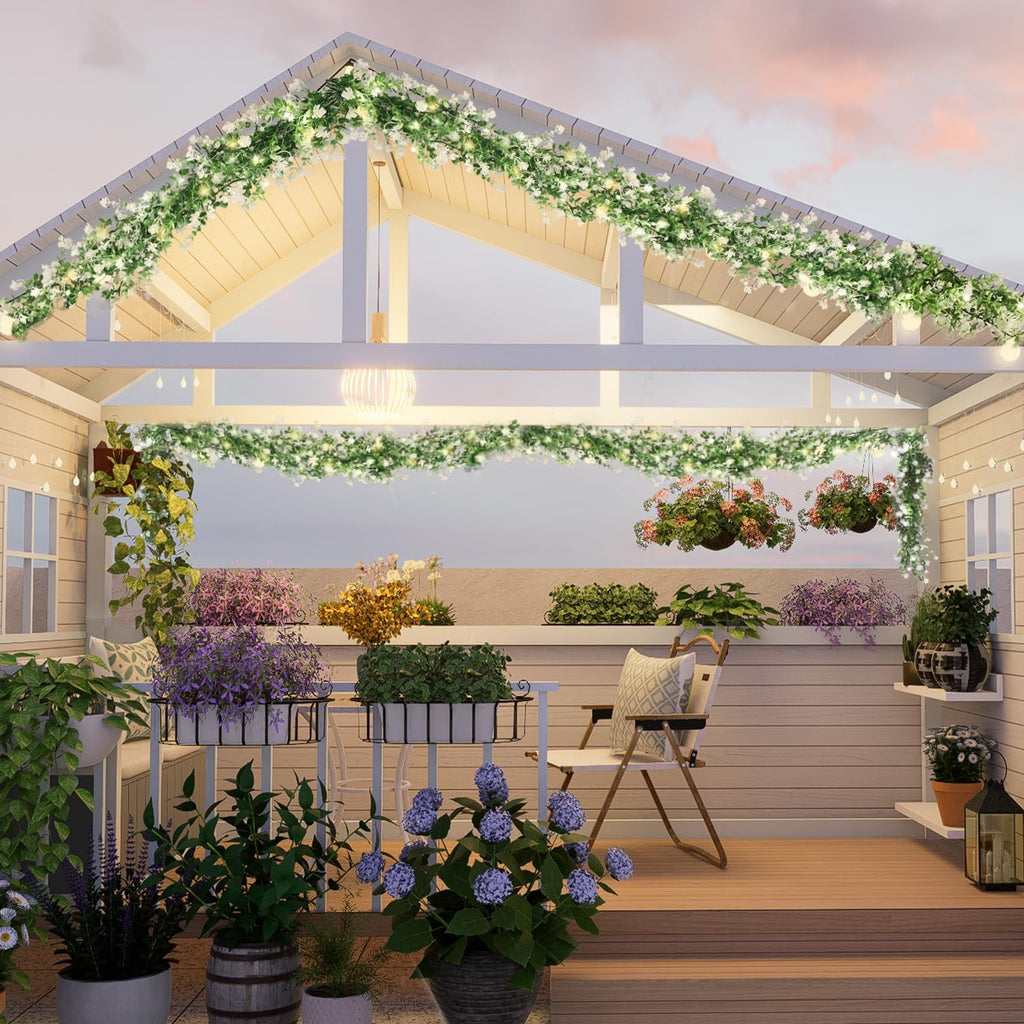 Artificial eucalyptus garland with LED lights draped along a porch roof and railing, surrounded by potted plants.
