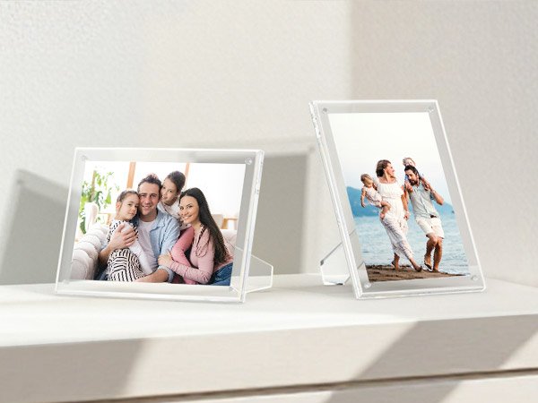 Two clear acrylic picture frames displaying family photos on a white shelf.