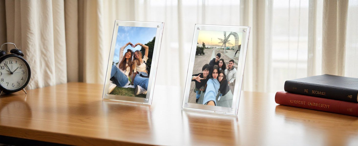 Two clear acrylic picture frames displaying photos of friends on a wooden desk with an alarm clock and books.