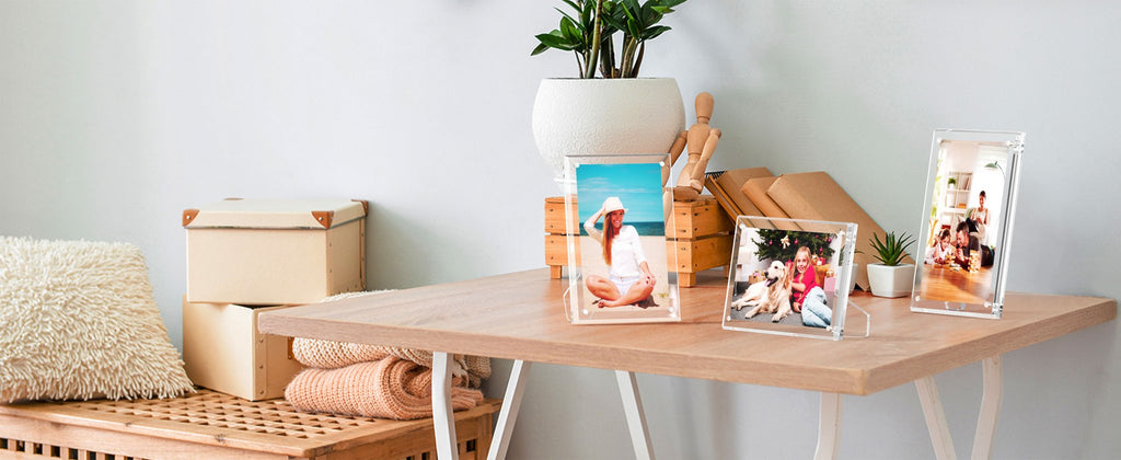 Three clear acrylic picture frames displaying photos on a wooden desk with decorative items.