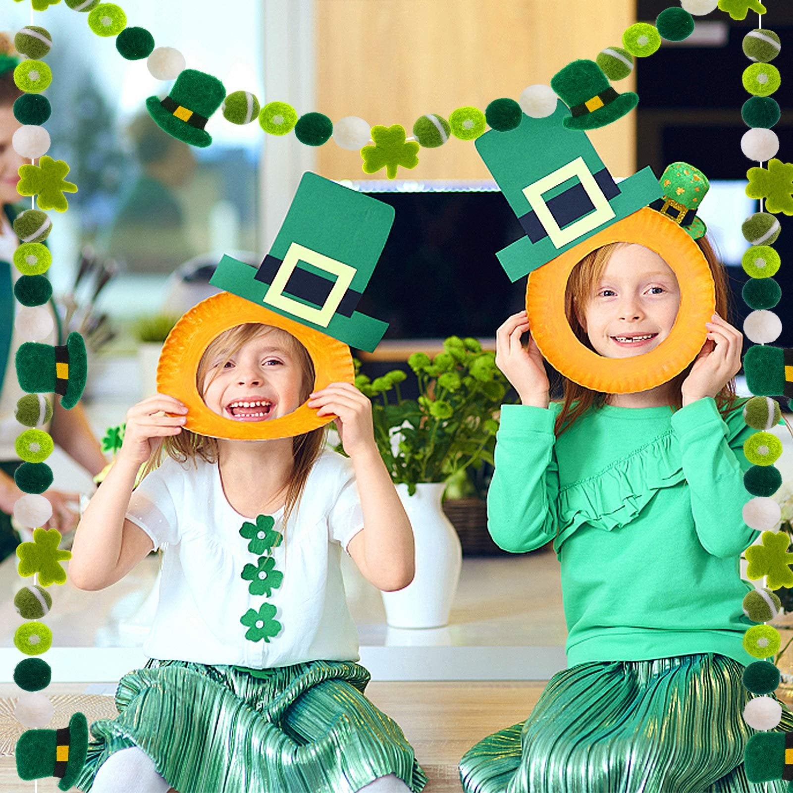 Two girls holding St. Patrick's Day themed paper frames in front of their faces, surrounded by felt garlands.