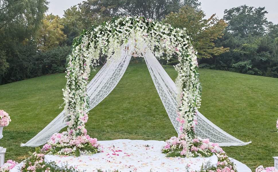 Wedding arch decorated with white and pink flowers and lace drapes on a grassy lawn.