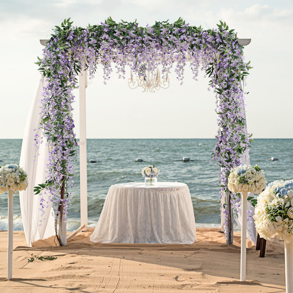 Wedding arch decorated with purple wisteria vines on a sandy beach with the ocean in the background.